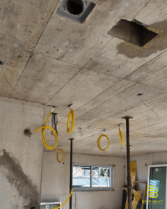 Yellow electrical wires hang from a cement ceiling at Jussy