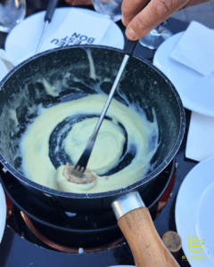 A hand holding a fork, scraping the leftovers of the fondue from the bouquet de chantier at Bief à Danse.