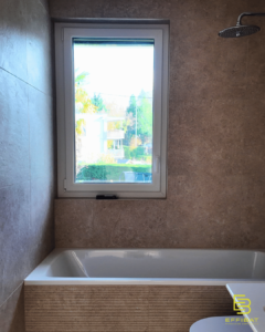 A window lets light in over a bathtub in a rose-colored bathroom.