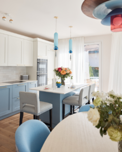The pastel blue of the kitchen with white cabinets and orange flowers