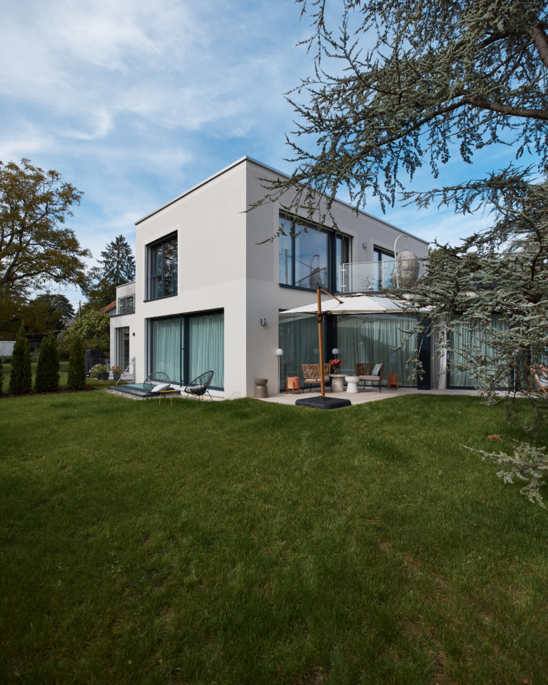 Vue de l'exterieur de la maison en crépi blanc et grand jardin vert